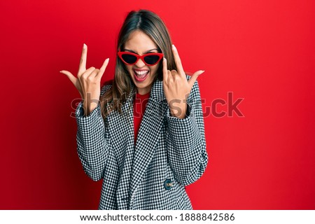 Young brunette woman wearing fashion and modern look shouting with crazy expression doing rock symbol with hands up. music star. heavy concept. 