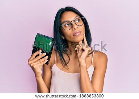 Young african american woman holding hard disk serious face thinking about question with hand on chin, thoughtful about confusing idea 