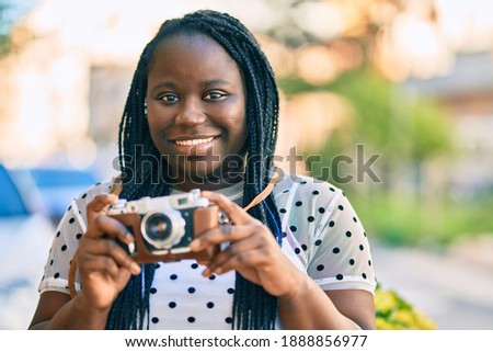 Young african american tourist woman smiling happy using vintage camera at the city.