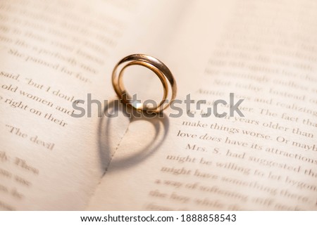 Two wedding rings on the book cast shadows in the form of hearts. Valentine's Day. Romance. Royalty-Free Stock Photo #1888858543