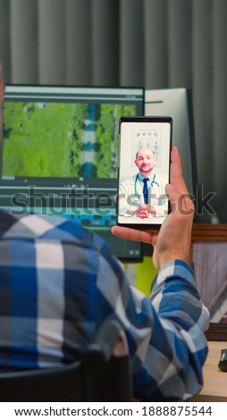 Disabled freelance videographer talking on video call with doctor in work time while creates content sitting in wheelchair in modern company office. Creator blogger working from photo studio.