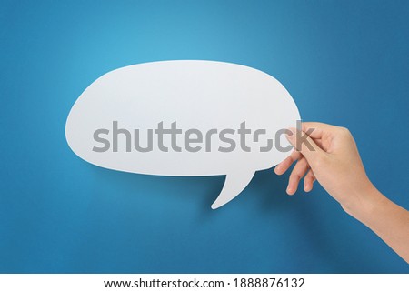 Hand holding an empty speech bubble at blue background.
