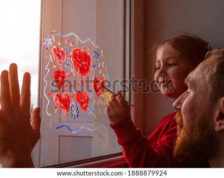 Child with father painting Love sign, playing indoors quarantine family leisure. Little girl holds paintbrush in hand draws red heart on window glass. Valentine's day. Stay home art concept New normal