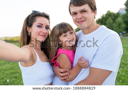 Happy family man dad woman mom, hug baby daughter and hold in her arms. Taking pictures smartphone, happy joyful posing relaxing, summer nature. Casual white clothes, pink T-shirt parenting concept
