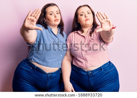 Young plus size twins wearing casual clothes doing frame using hands palms and fingers, camera perspective 