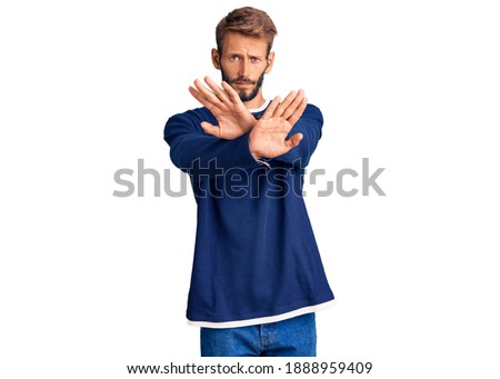 Handsome blond man with beard wearing casual sweater rejection expression crossing arms doing negative sign, angry face 