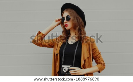 Portrait of stylish young woman photographer with vintage film camera wearing a boho style on a gray background