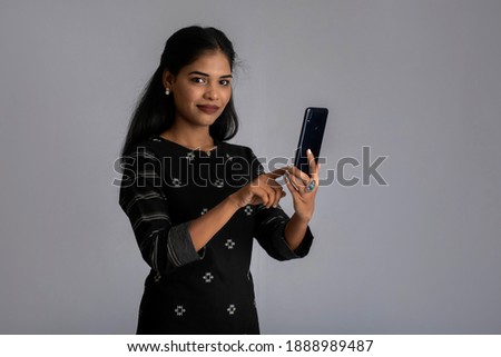 Young Indian girl using mobile phone or smartphone on gray background