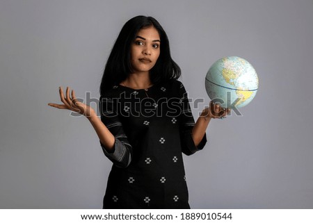 young girl holding the world globe and posing on a grey background.