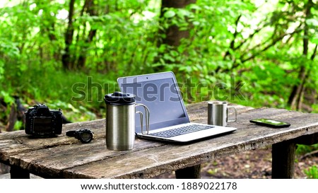 Close-up photo of a laptop, camera, coffee and smartphone on a wooden table outdoors.