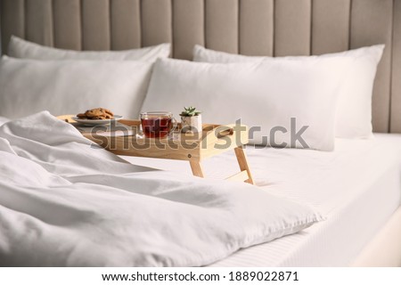 Wooden tray with breakfast and book near soft blanket on bed Royalty-Free Stock Photo #1889022871