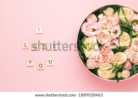 I love you lettering on the wooden squares with letters on the pink background and big round box with red flowers and roses. Greeting card concept.
