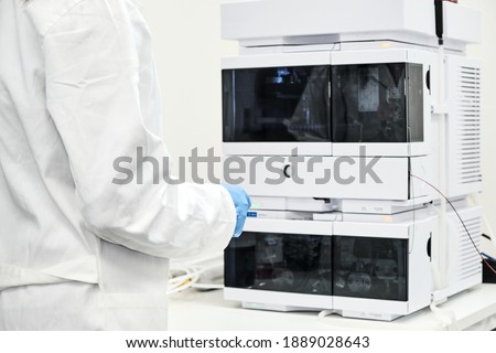 Scientist in rubber gloves and white lab coat standing near high performance liquid chromatography HPLC for separation organic compounds. Analytical chemistry laboratory. Analyzing process. Royalty-Free Stock Photo #1889028643
