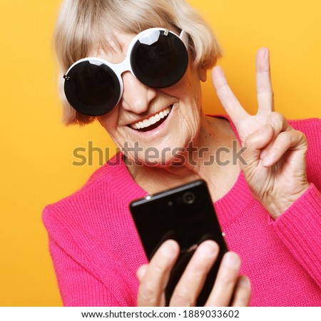 lifestyle, tehnology and people concept: Elderly lady holding a smartphone and making v-sign