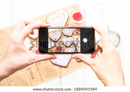 Hands with the phone close-up pictures homemade cookies for valentine's day sprinkled with hearts on a light background