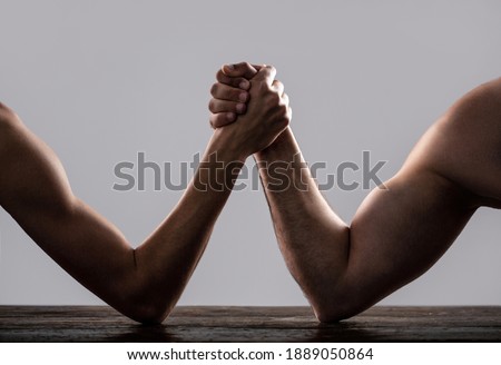 Arm wrestling. Heavily muscled man arm wrestling a puny weak man. Arms wrestling thin hand and a big strong arm in studio. Two man's hands clasped arm wrestling, strong and weak, unequal match.
