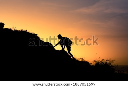 Mountain man silhouette climbing up a steep edge of mountain. People reaching life goals, and never giving up concept.  Royalty-Free Stock Photo #1889051599