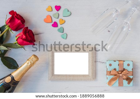 wooden background with roses, hearts, glasses of champagne, champagne, photo frame, copy space