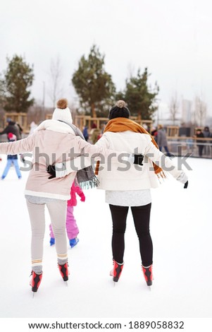 Soft focus vertical photo of two sisters girlfriends skating on an ice rink wearing hats and scarves. Winter active sport and friendship background