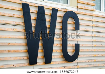 Large letters WC on facade of building with wood paneling. Public toilet sign in a city park. International restroom symbol. Outdoor WC, washroom.