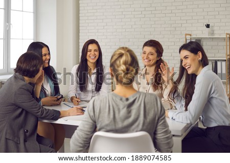 Team of happy young business women sitting around office table, discussing ideas, sharing funny stories and laughing. Group of smiling company employees talking and having fun in corporate meeting Royalty-Free Stock Photo #1889074585