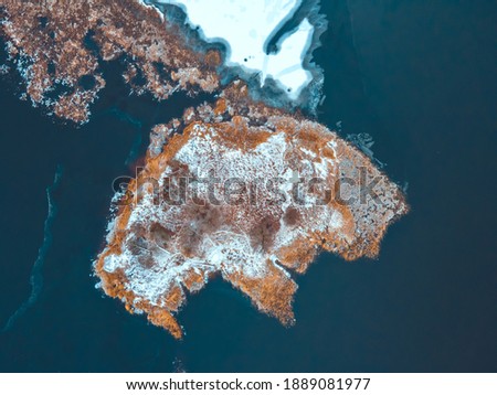 bird's-eye view of the island,the island is covered with snow and the coast is covered with yellow reeds