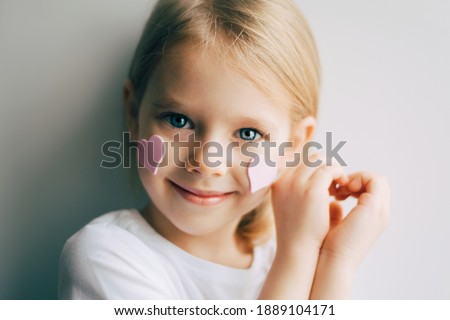 Pretty smilling blue-eyed blonde little  girl show heart shape symbol with hands. Child and valentines day. Love. Pink hearts on a face.