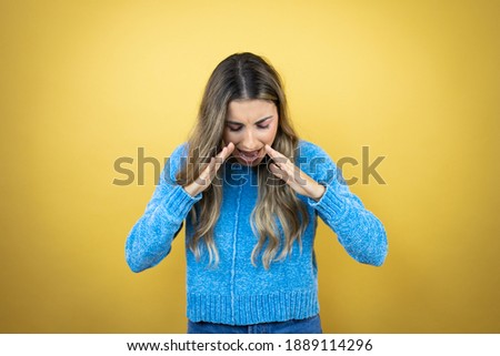 Pretty blonde woman with long hair standing over yellow background shouting and screaming loud down with hands on mouth