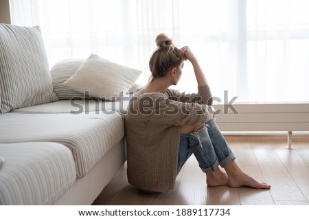 A depressed woman is sitting on the floor in the living room. Royalty-Free Stock Photo #1889117734