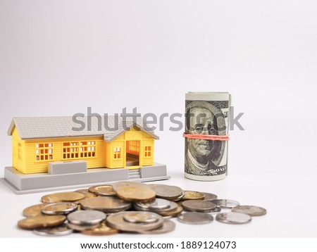 Selective focus photo of house miniature with dollar bills and coins isolated on white background.Concept of mortgage, construction, rental housing.