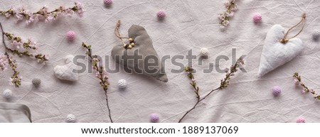 Hand made textile hearts and balls on cotton background. Monochromatic look, panoramic banner composition. Textile handicraft in neutral colors. Winter cherry flower twigs.