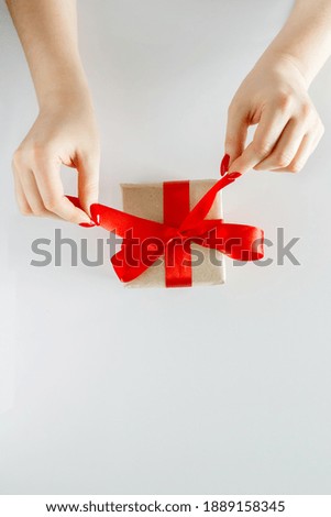  Valentine's Day gift in woman's hands - giftbox in craft paper and a red satin ribbon.