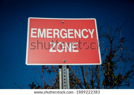 Red sign with white letters stating Emergency Zone against a blue sky