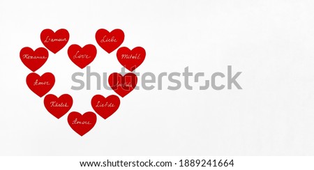Red paper hearts with white handwritten text. Translation Spanish, Italian, French, Russian, Ukrainian, German, Dutch, Polish, Swedish words is «love». Banner, copy space.