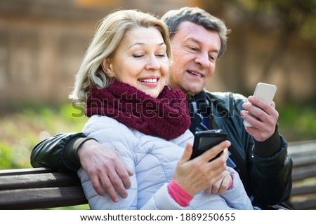Joyful smiling elderly couple exchanging phone numbers during outdoor date. Royalty-Free Stock Photo #1889250655