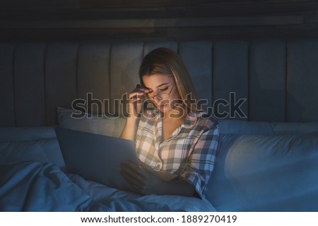 Young woman using laptop in bed at night. Sleeping disorder problem