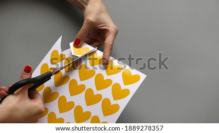 Someone cutting a heart out of paper and making postcard using scissors. Valentines day concept. Applique. Application. Grey and yellow colors.
