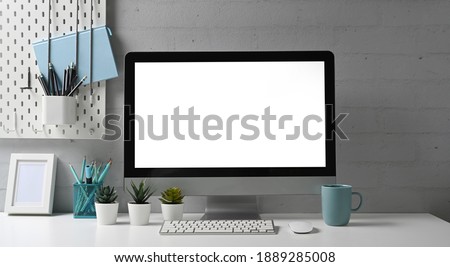 Front view of stylish workspace with mock up computer and office supplies gadget. Blank screen for graphic display montage.
