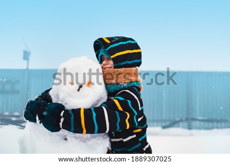 Children's winter games. A child has made a snowman and is hugging it.