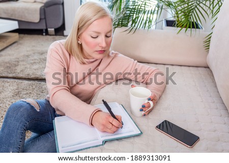Young woman studying and drinking coffee, Studious young woman working at home sitting on the floor in the living room with a class notes in binders studying for university