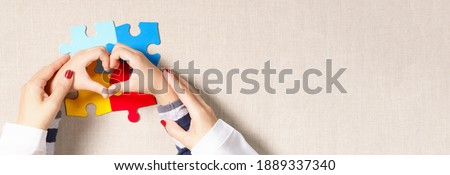 World autism awareness day, understanding - love concept, a beautiful mother holding hands of an autistic child making heart shape over symbol colored puzzle. ASD, April 2, Top view banner, copy space