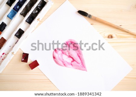 Flatlay with picture of red heart drawn by watercolors, with paints  and brush at wooden table background