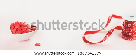 Heart shaped red sprinkles in a white bowl and gift ribbon roll, festive love gift and Valentine's Day concept or wedding day. wide banner. Small hearts. Selective focus