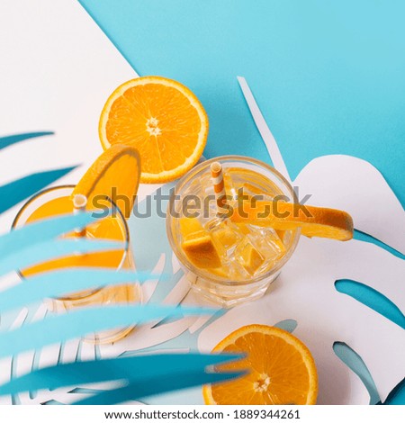 Cold orange juice drink in glass, fresh citrus and palm leaves on blue and white background. Healthy drink, copy space. Tropical summer concept. 