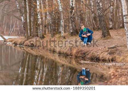 Happy family, father with daughter stand by the lake in spring. Wearing jackets and hats. Friendly family concept.