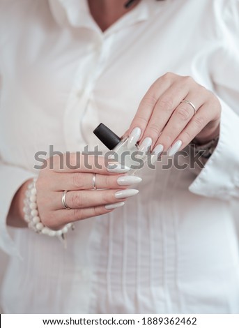 beautiful woman hands with long nails light white manicure and a bottle of nail polish