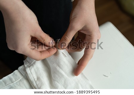 Close-up of a dressmaker's hands sew white cotton fabric for a dress with a needle and thread. Sewing Studio. Copy space.