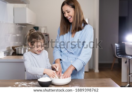 mom and daughter together in the kitchen knead dough in a bowl. Cooking concept together at home. Copy space.