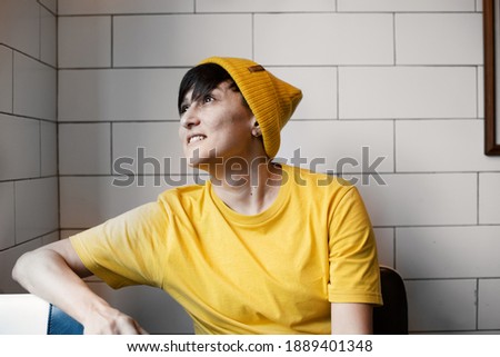 Young hipster woman in yellow hat and shirt is sitting in Barbershop. Portrait. Illuminating yellow and ultimate gray. 