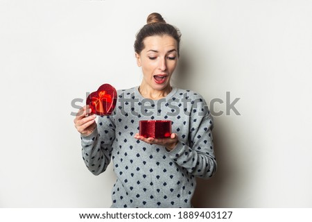 Surprised young woman rejoices with a gift on a light background. Valentine's day, birthday. Banner.